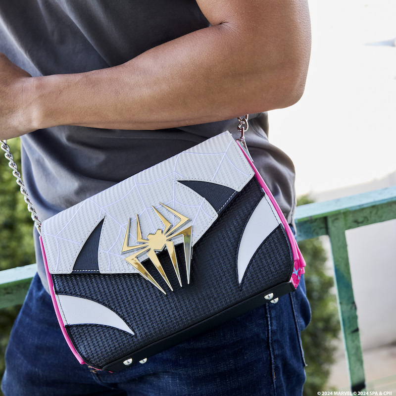 Man standing outside wearing the Loungefly Spider-Gwen crossbody bag, featuring a design that looks like her black and white suits. The bag has a metal spider over the clasp. 